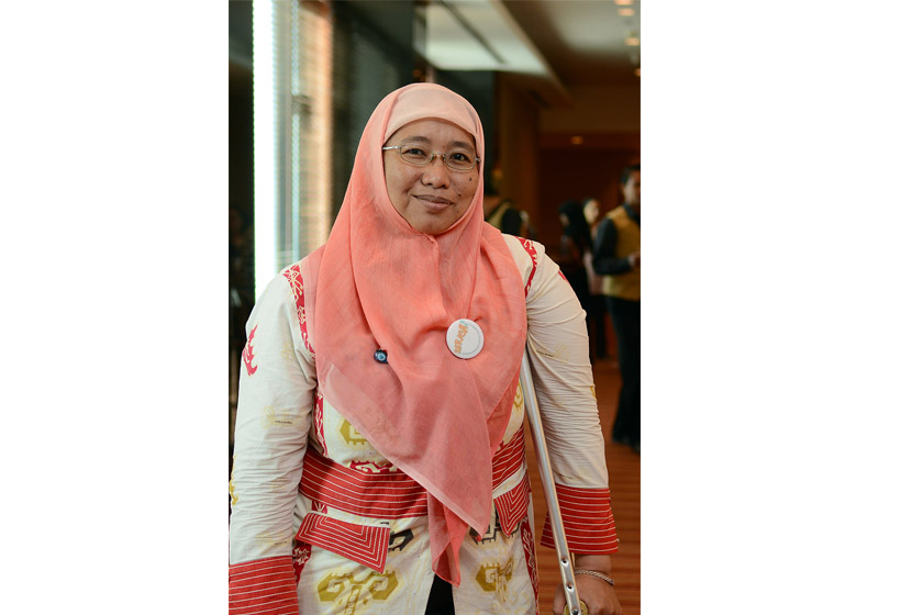 A woman with glasses and pink hijab is smiling